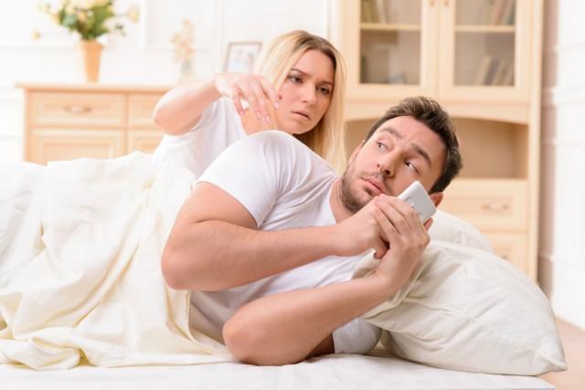 wife in bed with husband distracted by social media