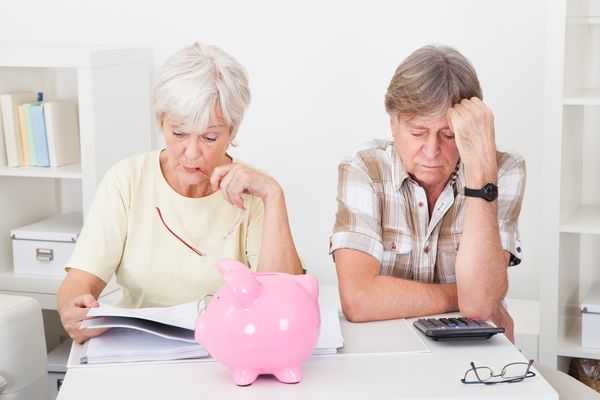 Bright pink piggy bank sits in front of an older couple each engrossed in thought.